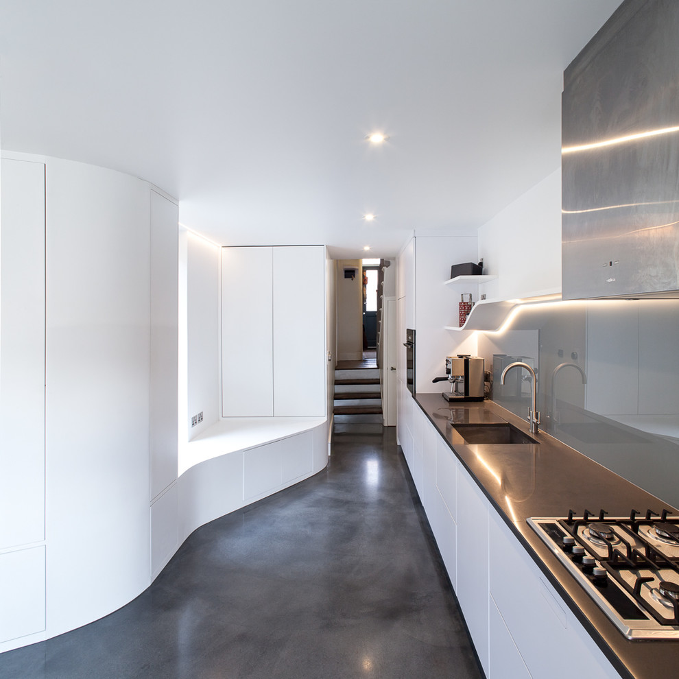 This is an example of a large contemporary single-wall kitchen in London with flat-panel cabinets, white cabinets, composite countertops, grey splashback, concrete flooring, grey floors, grey worktops, a single-bowl sink, glass sheet splashback and no island.