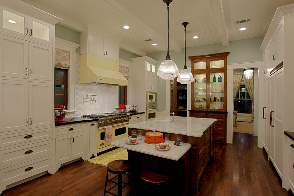Photo of a large classic galley kitchen/diner in Houston with coloured appliances, shaker cabinets, white cabinets, marble worktops, white splashback, stone slab splashback, an island, a submerged sink and dark hardwood flooring.