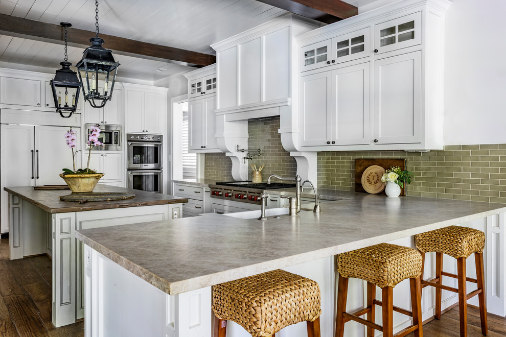 This is an example of a classic kitchen in Houston with a belfast sink, beaded cabinets, white cabinets, green splashback, metro tiled splashback, stainless steel appliances, medium hardwood flooring and an island.