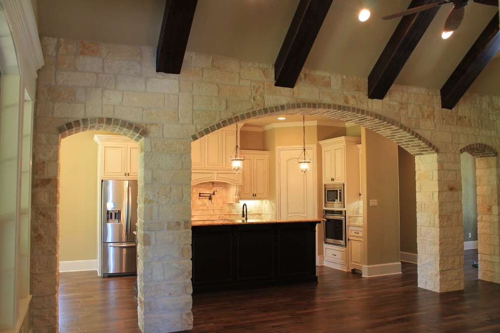 Example of a classic l-shaped eat-in kitchen design in Dallas with an undermount sink, raised-panel cabinets, distressed cabinets, granite countertops, beige backsplash, stone tile backsplash and stainless steel appliances