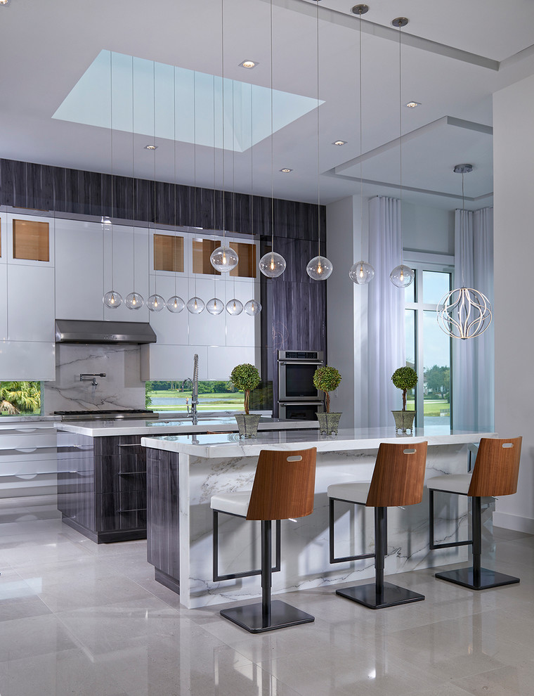 マイアミにあるコンテンポラリースタイルのおしゃれなマルチアイランドキッチン (アンダーカウンターシンク、フラットパネル扉のキャビネット、白いキャビネット、白いキッチンパネル、シルバーの調理設備、ベージュの床) の写真