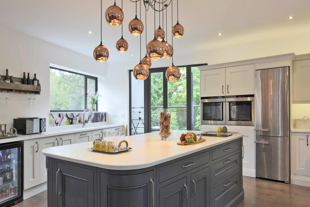 Design ideas for a traditional l-shaped kitchen in London with shaker cabinets, white cabinets, stainless steel appliances, dark hardwood flooring, an island and brown floors.