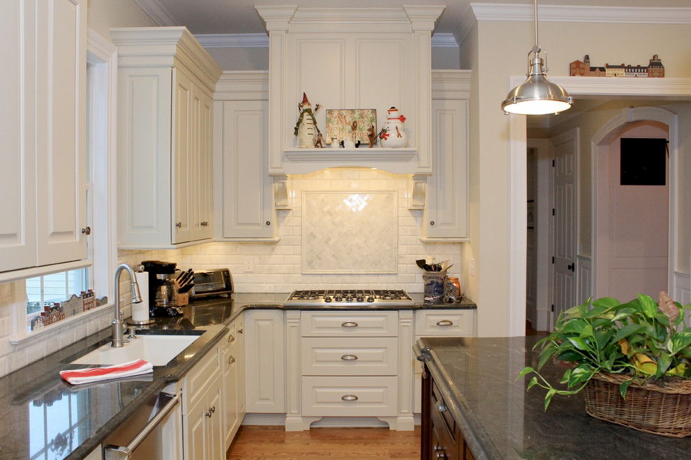 Foto på ett avskilt, stort vintage kök, med en undermonterad diskho, luckor med upphöjd panel, vita skåp, granitbänkskiva, vitt stänkskydd, stänkskydd i keramik, rostfria vitvaror, mellanmörkt trägolv och en köksö