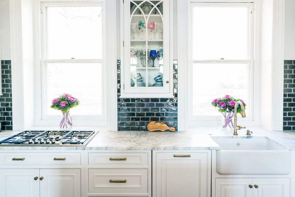 Mid-sized transitional l-shaped medium tone wood floor eat-in kitchen photo in Philadelphia with a farmhouse sink, glass-front cabinets, white cabinets, marble countertops, gray backsplash, ceramic backsplash, stainless steel appliances and an island