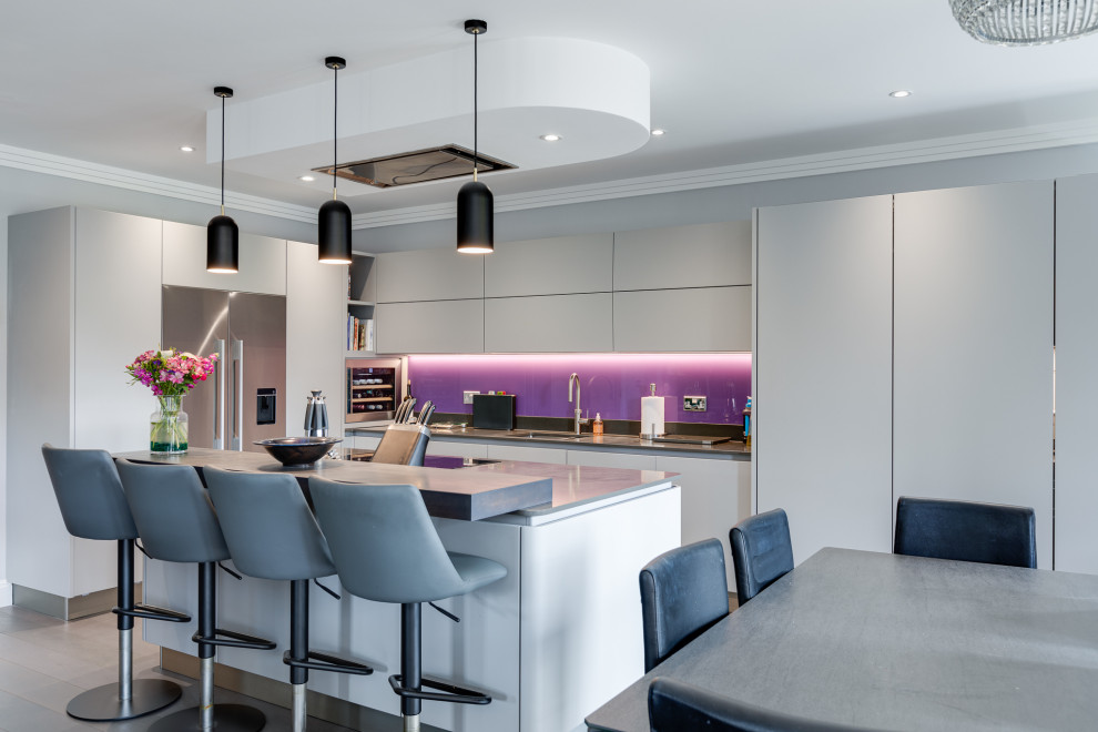 Inspiration for a contemporary l-shaped kitchen in Hertfordshire with a submerged sink, flat-panel cabinets, white cabinets, stainless steel appliances, an island, grey floors and grey worktops.