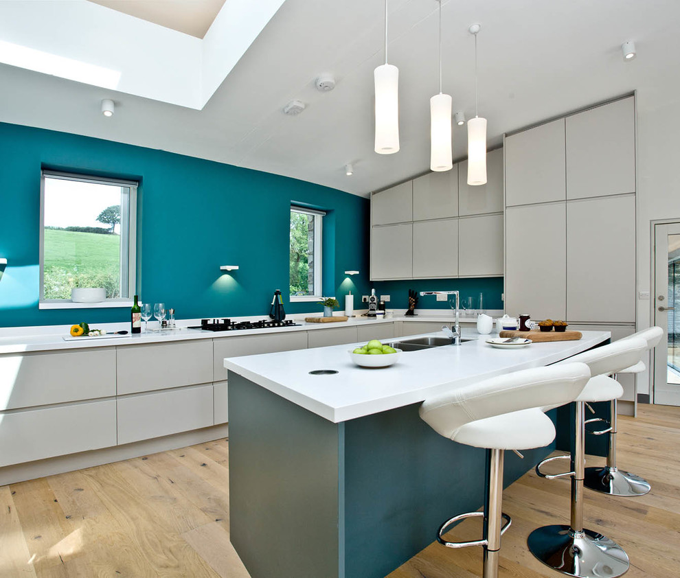 Moderne Küche in U-Form mit Doppelwaschbecken, flächenbündigen Schrankfronten, weißen Schränken, Küchenrückwand in Blau, hellem Holzboden, Halbinsel, beigem Boden und weißer Arbeitsplatte in Devon