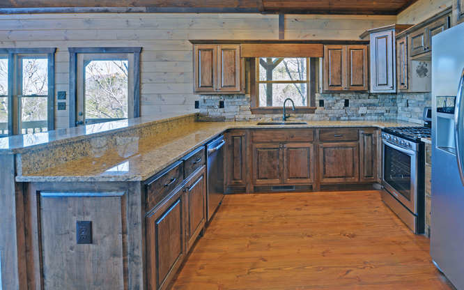 Inspiration for a medium sized rustic u-shaped enclosed kitchen in Atlanta with a submerged sink, raised-panel cabinets, granite worktops, stainless steel appliances, distressed cabinets, beige splashback, stone tiled splashback, medium hardwood flooring, a breakfast bar and brown floors.