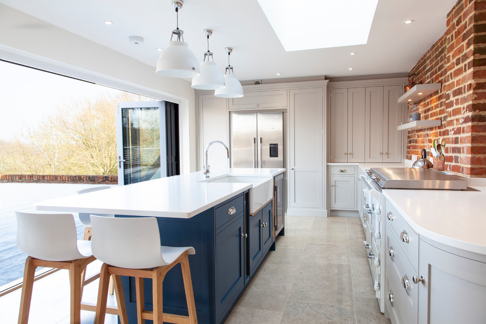 This is an example of a traditional u-shaped enclosed kitchen in Essex with a belfast sink, shaker cabinets, white cabinets, brick splashback, stainless steel appliances, an island and white worktops.