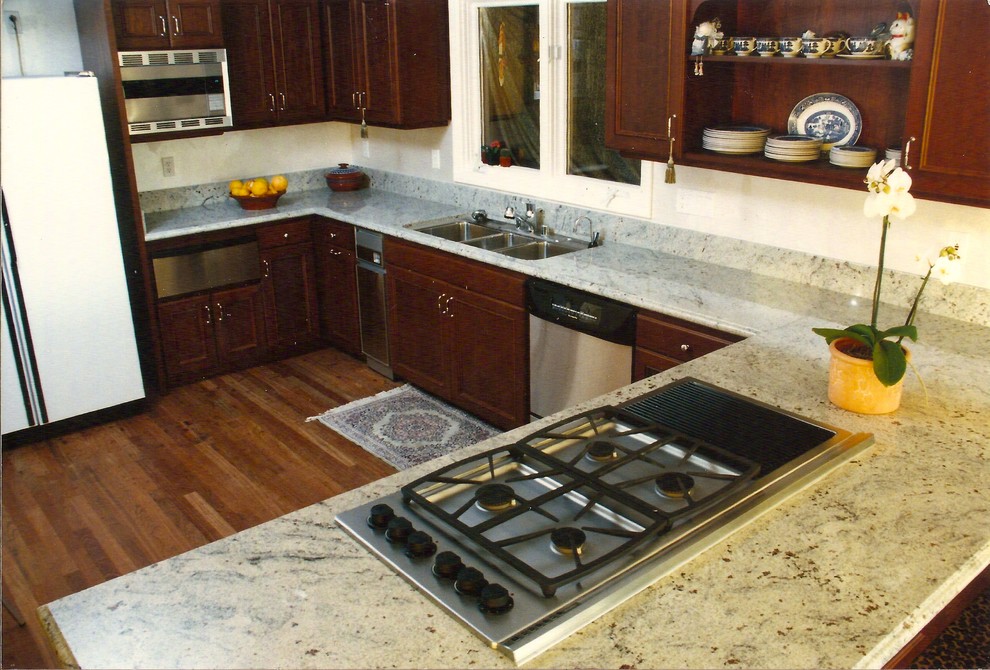 Example of a mid-sized transitional u-shaped medium tone wood floor and brown floor enclosed kitchen design in Hawaii with a triple-bowl sink, recessed-panel cabinets, dark wood cabinets, granite countertops, stainless steel appliances, a peninsula and white countertops