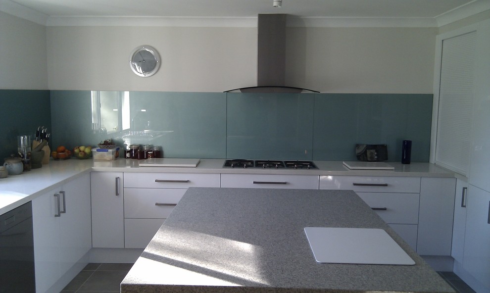 This is an example of a medium sized modern u-shaped kitchen/diner in Wollongong with a double-bowl sink, flat-panel cabinets, white cabinets, engineered stone countertops, green splashback, glass sheet splashback, stainless steel appliances, terracotta flooring and an island.