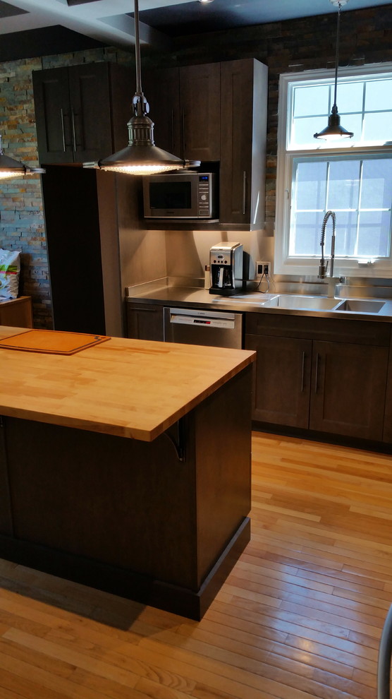 Inspiration for a mid-sized industrial l-shaped light wood floor enclosed kitchen remodel in Ottawa with a double-bowl sink, shaker cabinets, gray cabinets, stainless steel countertops, metallic backsplash, stone tile backsplash, stainless steel appliances and an island