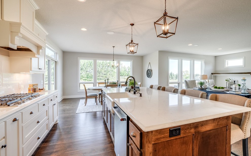 Large transitional galley medium tone wood floor and brown floor open concept kitchen photo in Minneapolis with a farmhouse sink, beaded inset cabinets, white cabinets, quartz countertops, white backsplash, subway tile backsplash, stainless steel appliances and an island
