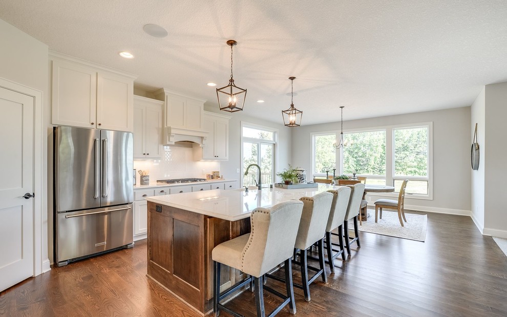 Inspiration for a large transitional galley medium tone wood floor and brown floor open concept kitchen remodel in Minneapolis with a farmhouse sink, white cabinets, quartz countertops, white backsplash, subway tile backsplash, stainless steel appliances, an island and shaker cabinets