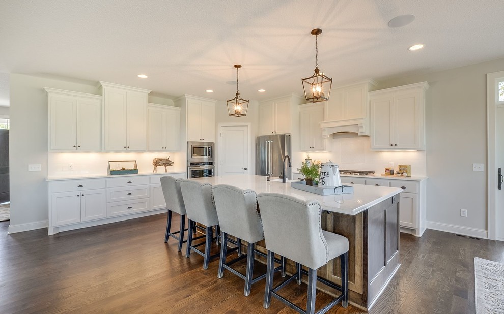 Example of a large transitional galley medium tone wood floor and brown floor open concept kitchen design in Minneapolis with a farmhouse sink, beaded inset cabinets, white cabinets, quartz countertops, white backsplash, subway tile backsplash, stainless steel appliances and an island