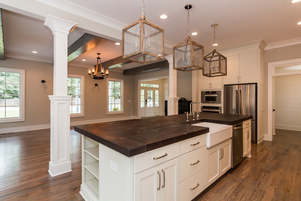 Example of a large country l-shaped medium tone wood floor kitchen design in Raleigh with a farmhouse sink, flat-panel cabinets, white cabinets, wood countertops, gray backsplash, ceramic backsplash, stainless steel appliances and an island