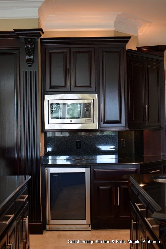 マイアミにある広いトラディショナルスタイルのおしゃれなアイランドキッチン (濃色木目調キャビネット、御影石カウンター、黒いキッチンパネル、シルバーの調理設備、磁器タイルの床) の写真