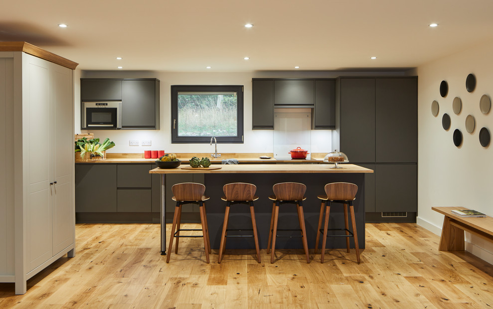 This is an example of a contemporary kitchen in London with flat-panel cabinets, grey cabinets, white splashback, glass sheet splashback, integrated appliances, light hardwood flooring, an island, beige floors and beige worktops.