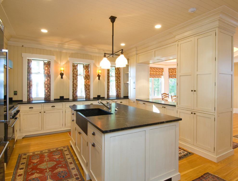Mid-sized elegant u-shaped light wood floor eat-in kitchen photo in Boston with a farmhouse sink, recessed-panel cabinets, white cabinets, soapstone countertops, stainless steel appliances and an island