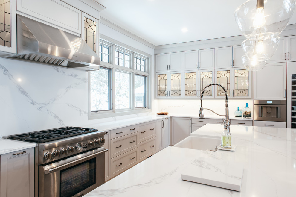 Eat-in kitchen - transitional u-shaped eat-in kitchen idea in Toronto with a farmhouse sink, flat-panel cabinets, white cabinets, solid surface countertops, white backsplash, stainless steel appliances, an island and white countertops