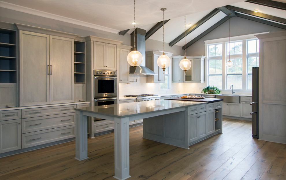 Photo of a large classic u-shaped kitchen in Wilmington with a submerged sink, beaded cabinets, grey cabinets, engineered stone countertops, white splashback, metro tiled splashback, stainless steel appliances, medium hardwood flooring, an island and brown floors.