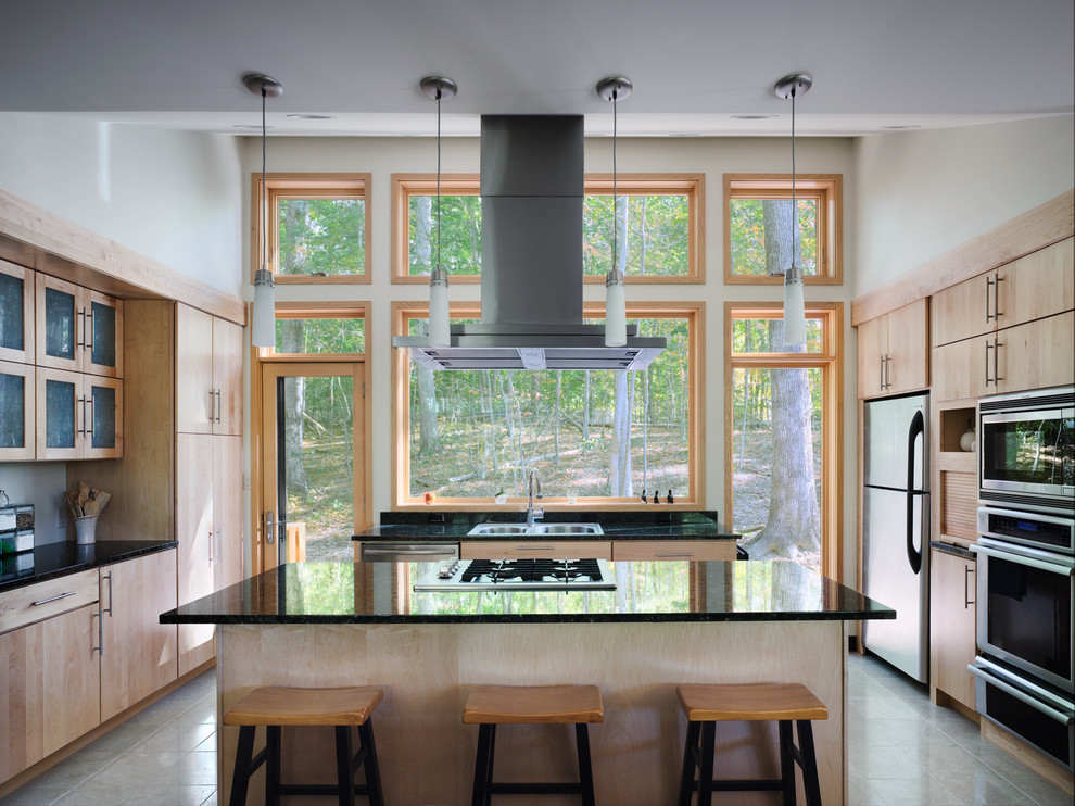 Inredning av ett modernt litet kök, med en nedsänkt diskho, luckor med glaspanel, skåp i ljust trä, granitbänkskiva, svart stänkskydd, stänkskydd i sten, rostfria vitvaror, travertin golv och en köksö