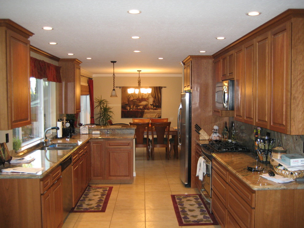 Exempel på ett mellanstort klassiskt kök, med en dubbel diskho, grått stänkskydd, rostfria vitvaror, klinkergolv i keramik, beiget golv, luckor med upphöjd panel, skåp i mellenmörkt trä, granitbänkskiva och stänkskydd i sten