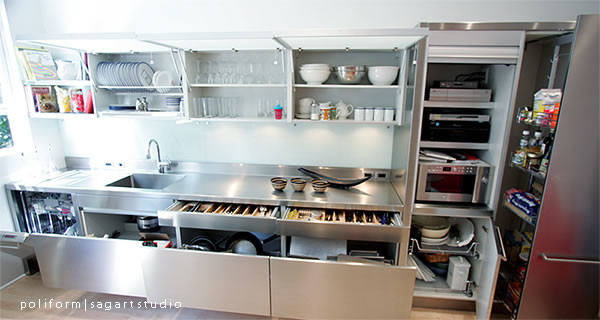 Foto på ett funkis linjärt kök och matrum, med en integrerad diskho, släta luckor, skåp i rostfritt stål, bänkskiva i rostfritt stål, vitt stänkskydd, rostfria vitvaror, glaspanel som stänkskydd och ljust trägolv
