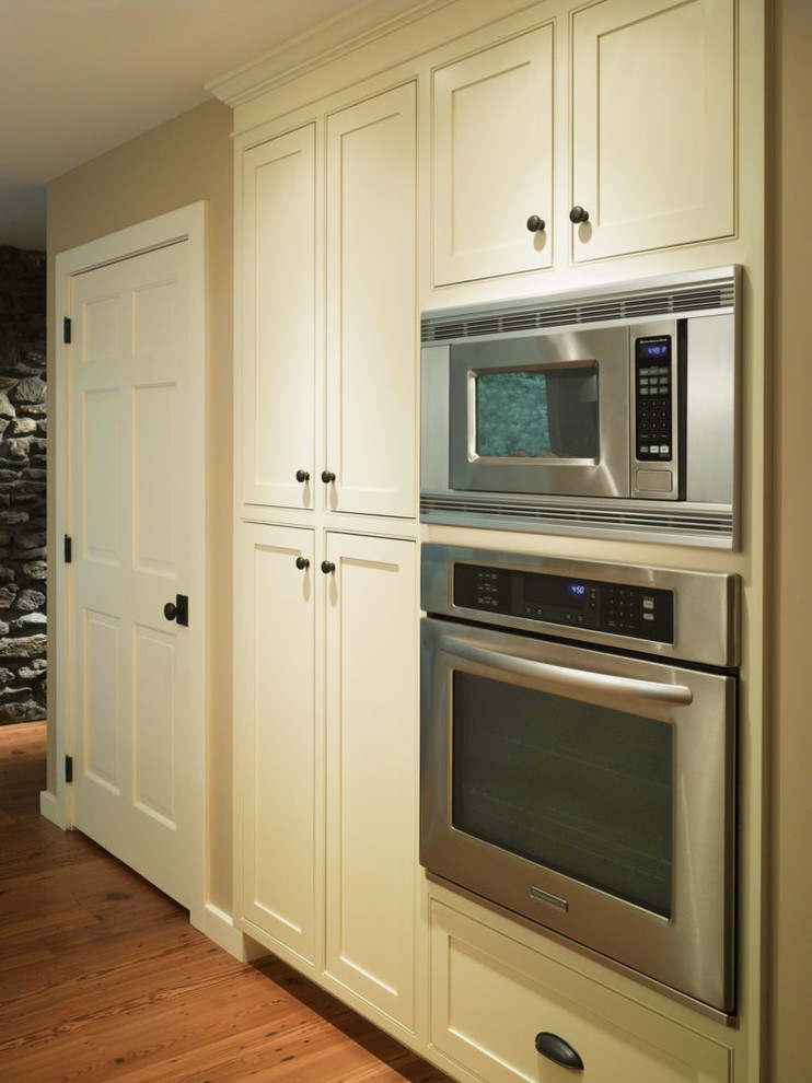 Bild på ett mellanstort lantligt linjärt kök och matrum, med en rustik diskho, skåp i shakerstil, vita skåp, svart stänkskydd, stänkskydd i sten, integrerade vitvaror och en köksö