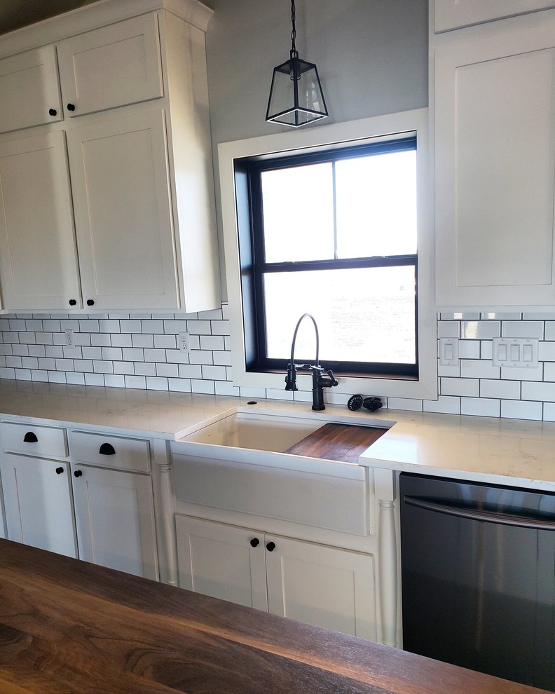 Inspiration for a mid-sized cottage l-shaped vinyl floor and gray floor eat-in kitchen remodel in Kansas City with a farmhouse sink, flat-panel cabinets, white cabinets, quartz countertops, white backsplash, subway tile backsplash, stainless steel appliances, an island and white countertops