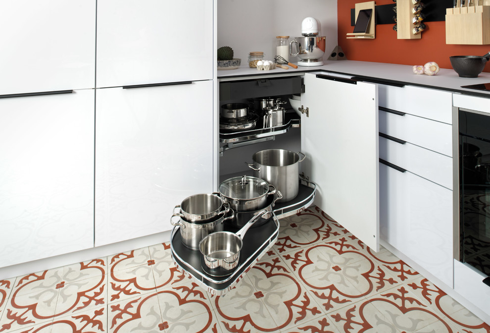 This is an example of a small modern u-shaped kitchen/diner in Surrey with a single-bowl sink, flat-panel cabinets, white cabinets, laminate countertops, orange splashback, stainless steel appliances, terracotta flooring, a breakfast bar, multi-coloured floors and white worktops.