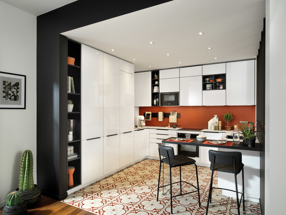 Inredning av ett modernt litet vit vitt u-kök, med en enkel diskho, släta luckor, vita skåp, laminatbänkskiva, orange stänkskydd, klinkergolv i terrakotta, en halv köksö, flerfärgat golv och svarta vitvaror