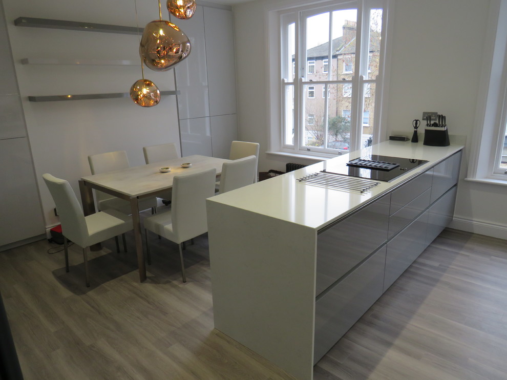 Design ideas for a medium sized contemporary single-wall kitchen/diner in London with a built-in sink, flat-panel cabinets, grey cabinets, quartz worktops, grey splashback, wood splashback, black appliances, vinyl flooring, an island, grey floors and white worktops.