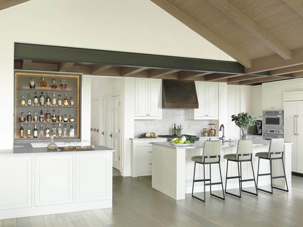 オースティンにあるトランジショナルスタイルのおしゃれなアイランドキッチン (シェーカースタイル扉のキャビネット、白いキャビネット、グレーのキッチンパネル、淡色無垢フローリング) の写真