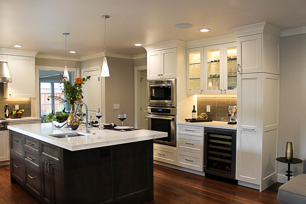 Exempel på ett stort klassiskt kök, med en undermonterad diskho, vita skåp, bänkskiva i kvarts, grått stänkskydd, stänkskydd i glaskakel, rostfria vitvaror, mellanmörkt trägolv, en köksö och luckor med infälld panel