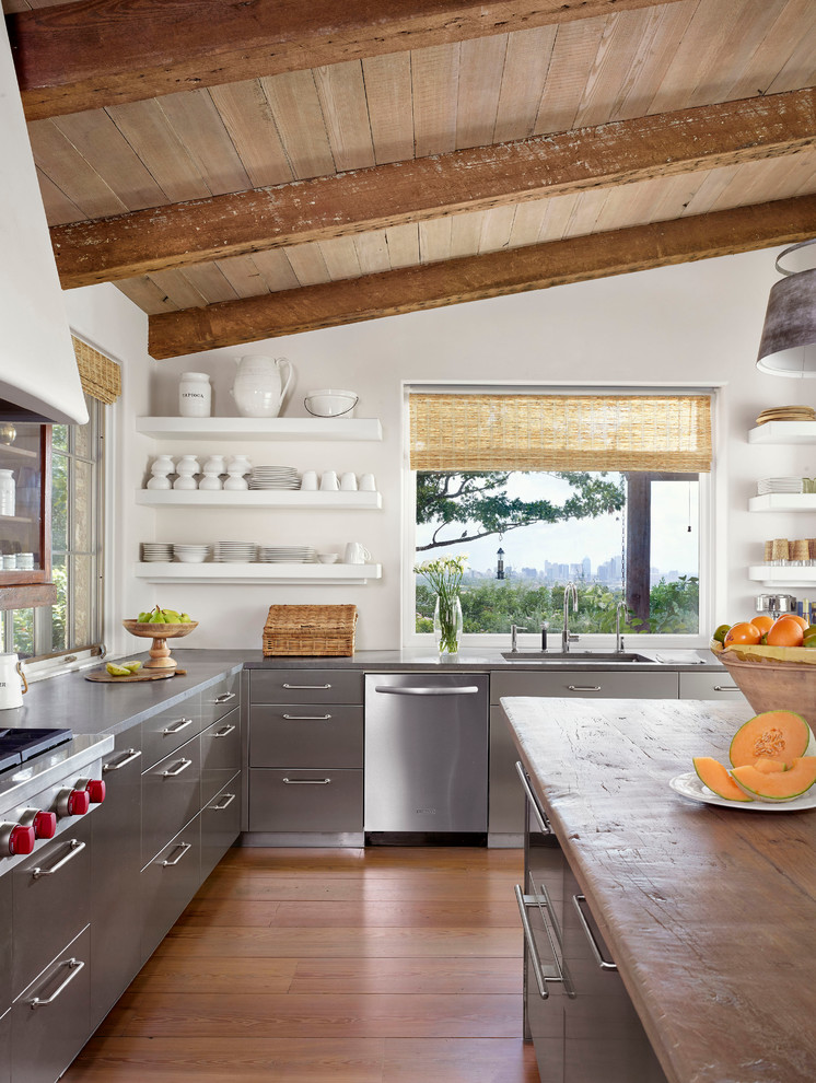 Foto på ett lantligt kök, med en undermonterad diskho, släta luckor, grå skåp, vitt stänkskydd, rostfria vitvaror, mellanmörkt trägolv och en köksö