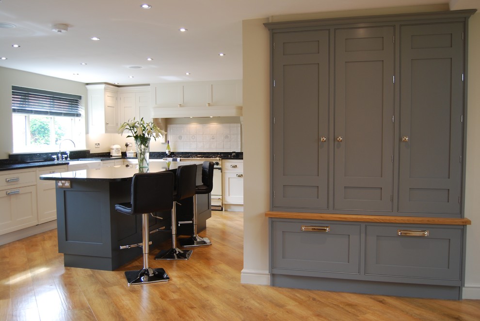 Example of a large minimalist u-shaped light wood floor eat-in kitchen design in West Midlands with a farmhouse sink, shaker cabinets, granite countertops, ceramic backsplash, colored appliances and an island