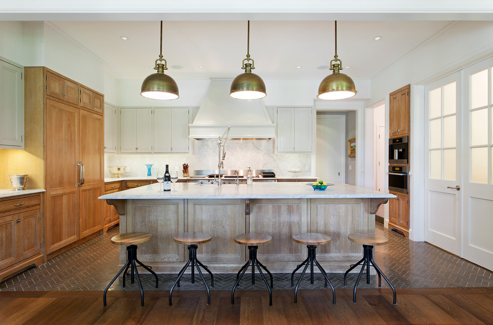 Example of a mid-sized classic u-shaped dark wood floor and brown floor open concept kitchen design in Austin with recessed-panel cabinets, medium tone wood cabinets, white backsplash, an island, quartzite countertops and stainless steel appliances