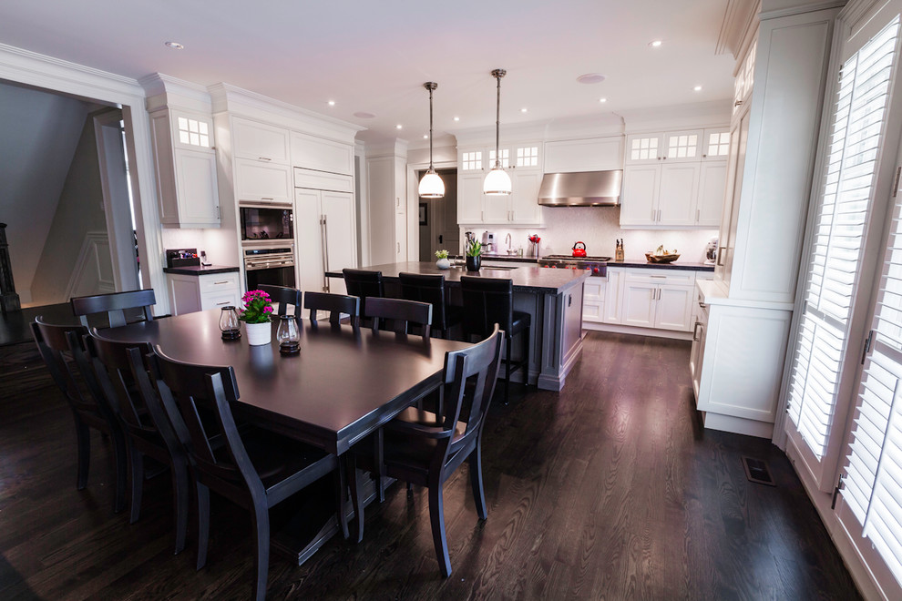 Example of a large transitional u-shaped dark wood floor open concept kitchen design in Toronto with an undermount sink, shaker cabinets, white cabinets, granite countertops, white backsplash, mosaic tile backsplash, paneled appliances and an island