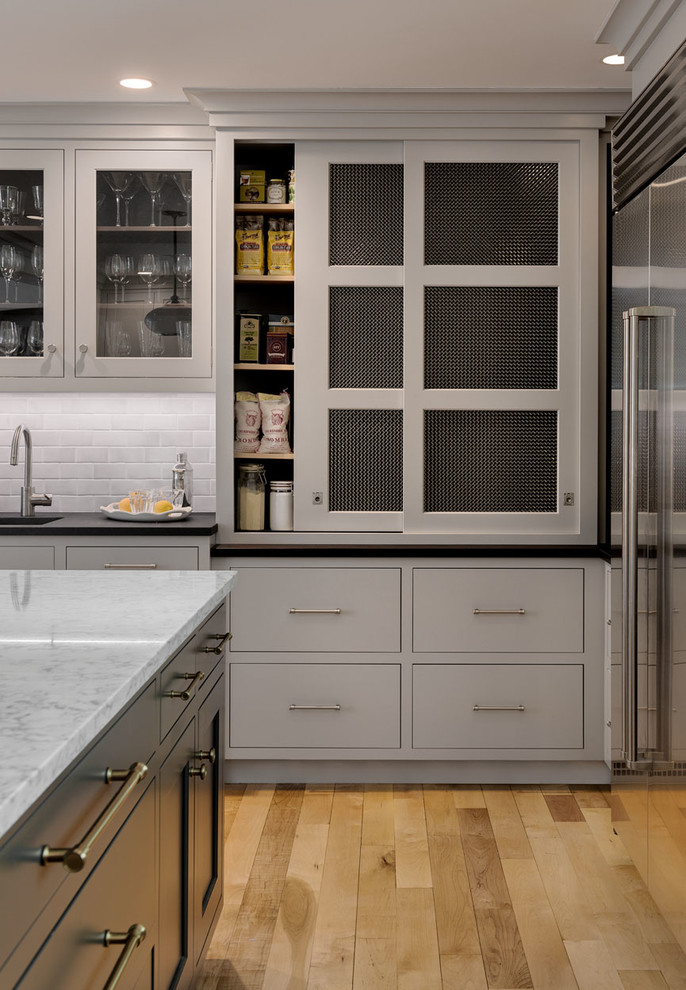 Bild på ett vintage grå grått kök, med en undermonterad diskho, luckor med profilerade fronter, grå skåp, marmorbänkskiva, grått stänkskydd, stänkskydd i tunnelbanekakel, rostfria vitvaror, ljust trägolv, en köksö och beiget golv