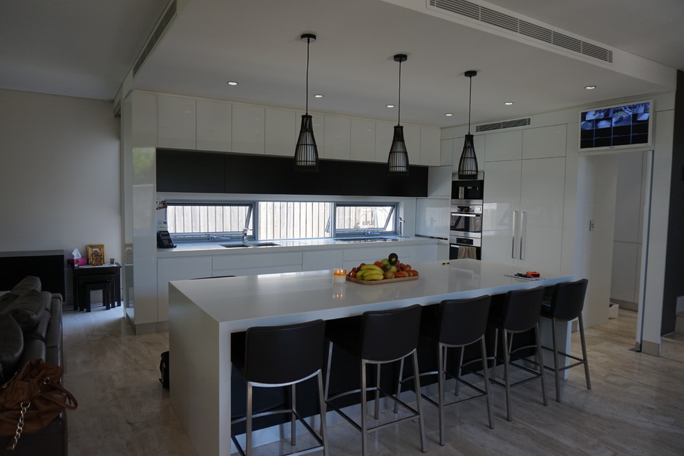 Foto på ett mellanstort funkis kök, med en undermonterad diskho, vita skåp, bänkskiva i kvarts, rostfria vitvaror, travertin golv och en köksö