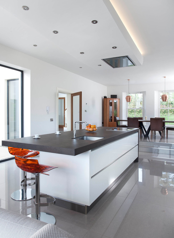 Photo of a large contemporary single-wall open plan kitchen in Belfast with an integrated sink, flat-panel cabinets, white cabinets, engineered stone countertops, grey splashback, stone slab splashback, stainless steel appliances, porcelain flooring and an island.