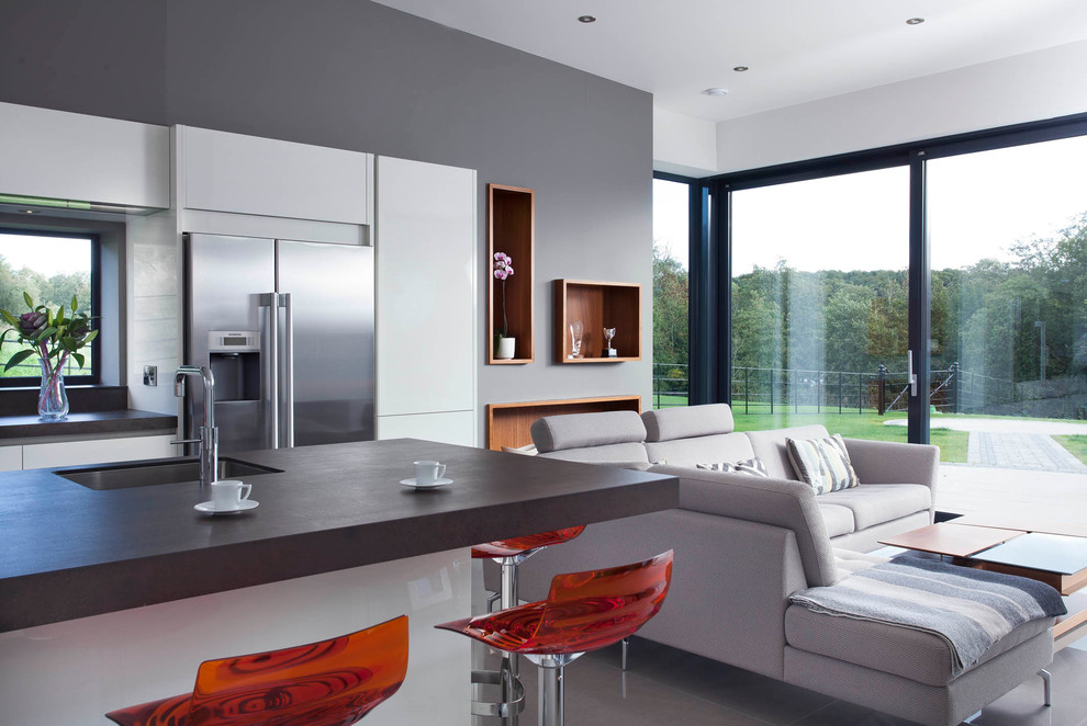 Design ideas for a large contemporary single-wall open plan kitchen in Belfast with an integrated sink, flat-panel cabinets, white cabinets, engineered stone countertops, grey splashback, stone slab splashback, stainless steel appliances, porcelain flooring and an island.
