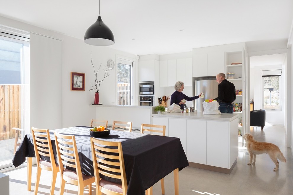 Imagen de cocina comedor actual con armarios con paneles lisos, puertas de armario blancas, electrodomésticos de acero inoxidable, suelo de cemento y península