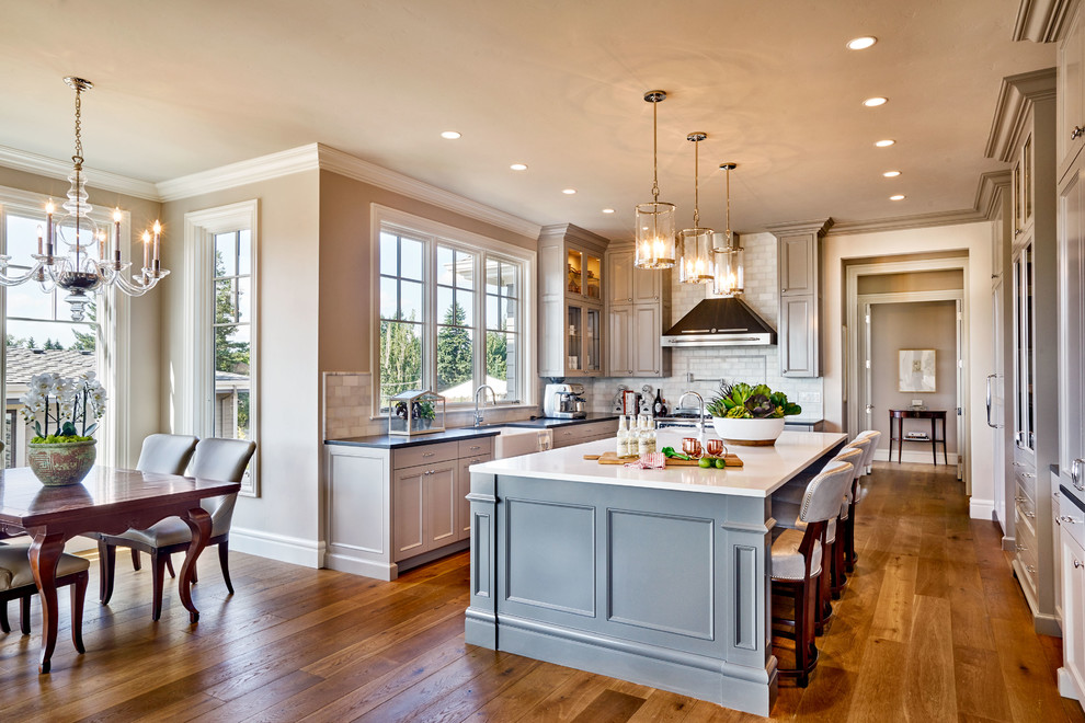 Inspiration for a large timeless u-shaped medium tone wood floor and brown floor eat-in kitchen remodel in Portland with a farmhouse sink, recessed-panel cabinets, gray cabinets, quartz countertops, gray backsplash, subway tile backsplash, paneled appliances and an island
