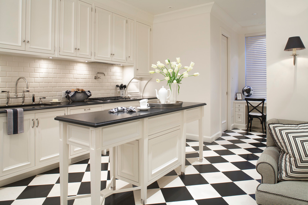 Bild på ett mellanstort vintage svart linjärt svart kök och matrum, med en dubbel diskho, luckor med infälld panel, vita skåp, bänkskiva i kalksten, vitt stänkskydd, stänkskydd i tegel, integrerade vitvaror, klinkergolv i keramik, en köksö och flerfärgat golv