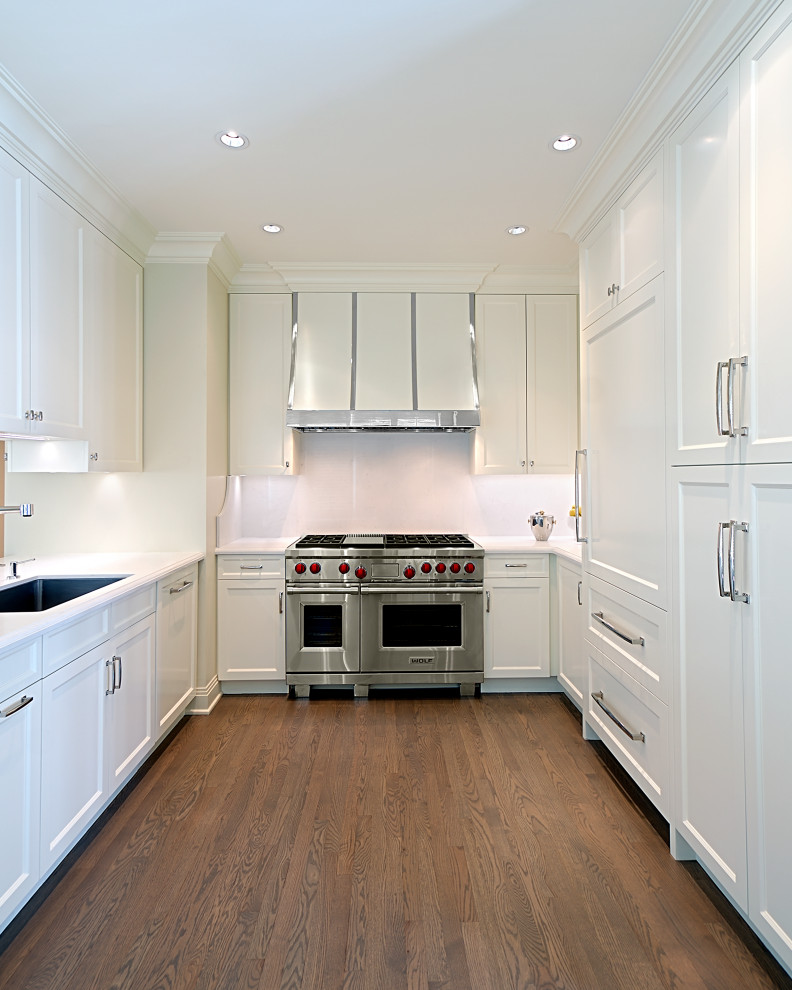 Small traditional u-shaped kitchen/diner in Chicago with a submerged sink, recessed-panel cabinets, white cabinets, engineered stone countertops, white splashback, engineered quartz splashback, stainless steel appliances, medium hardwood flooring, no island, brown floors and white worktops.