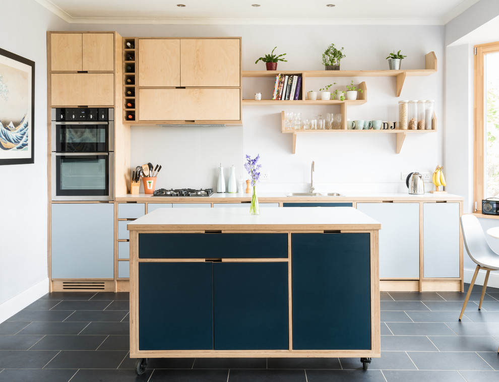 Foto på ett mellanstort funkis grå linjärt kök och matrum, med träbänkskiva, vitt stänkskydd, glaspanel som stänkskydd, rostfria vitvaror, en köksö, en nedsänkt diskho, släta luckor, blå skåp och svart golv