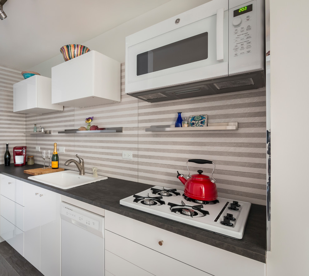 Photo of a small contemporary galley kitchen in New York with a built-in sink, flat-panel cabinets, white cabinets, composite countertops, multi-coloured splashback, porcelain splashback, white appliances, porcelain flooring, no island and grey floors.