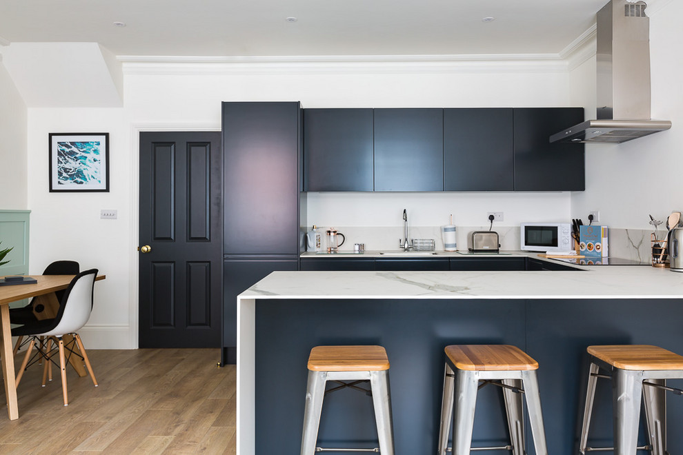 Inspiration for a contemporary u-shaped kitchen/diner in Essex with an integrated sink, flat-panel cabinets, black cabinets, light hardwood flooring, a breakfast bar and white worktops.