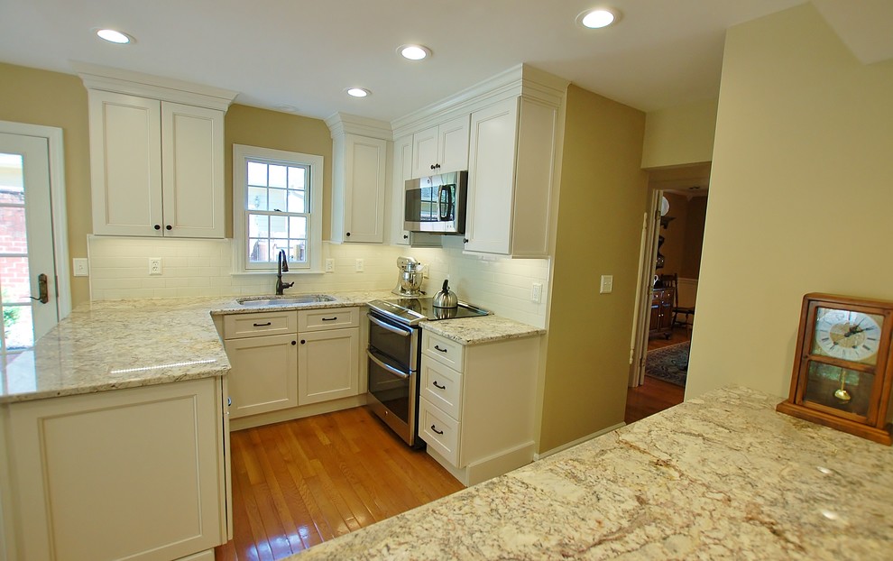 Example of a mid-sized transitional l-shaped light wood floor eat-in kitchen design in Philadelphia with an undermount sink, raised-panel cabinets, white cabinets, granite countertops, white backsplash, subway tile backsplash, stainless steel appliances and an island